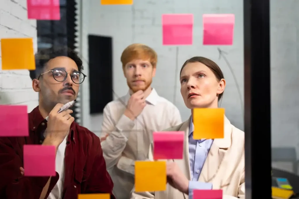 Grupo de profissionais analisando post-its coloridos em uma parede, discutindo estratégias para mapear interessados em um projeto.